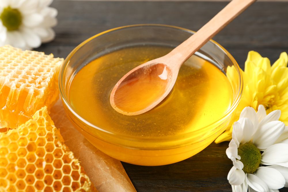 Flowers, glass bowl with honey and dipper on wooden background, closeup