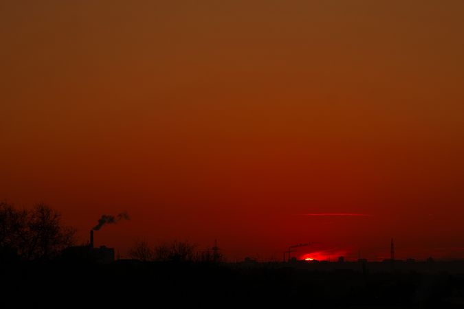 Fiery red sun dipping below horizon with industrial smoke