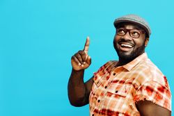 Portrait of a happy man in orange shirt smiling and pointing up, with blue copy space around him