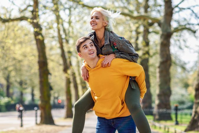 Male giving female friend piggy back ride in park