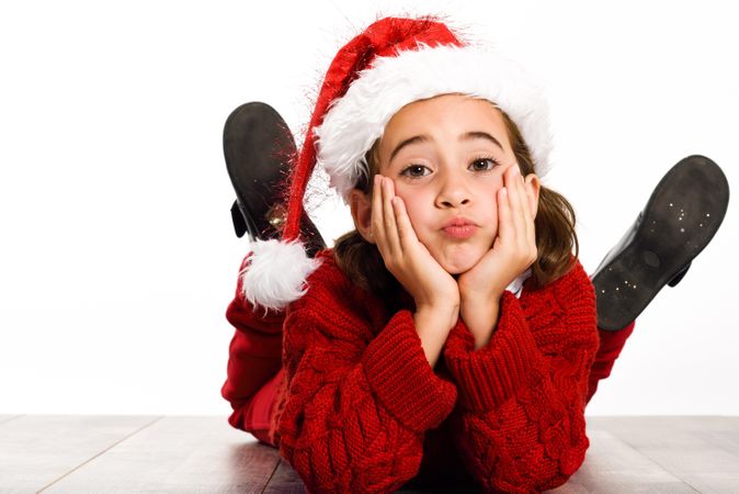 Girl in santa outfit lying on stomach on ground resting her head on her hands