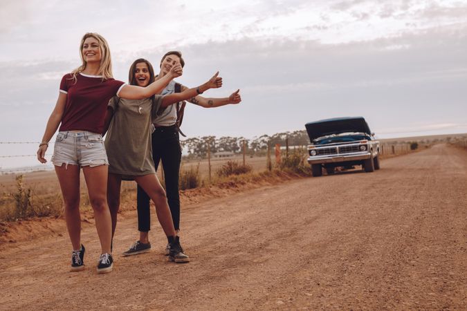 Three young women hitchhiking near their broken car on country road