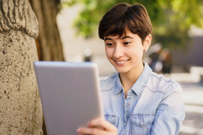 A Smiling Young Woman Fully Enjoying Her Tablet While Sitting Outdoors in the Bright Sunshine