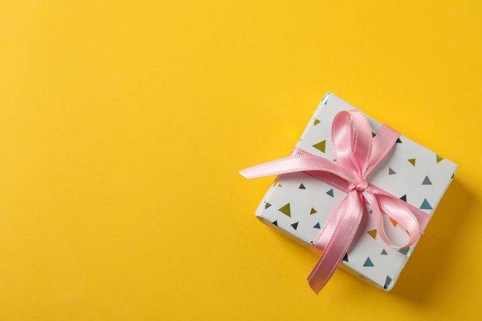 Gift box with bow on yellow background, space for text