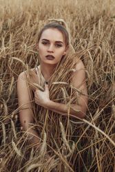 Young woman with purple make-up sitting in wheat field