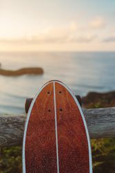 Surf skate leaning on wooden railing against blurred beach