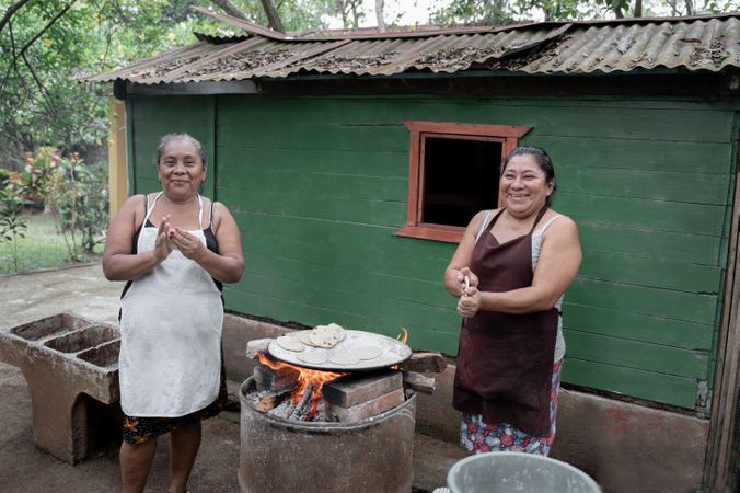 Two adult Hispanic women are smiling while shaping corn tortillas by hand