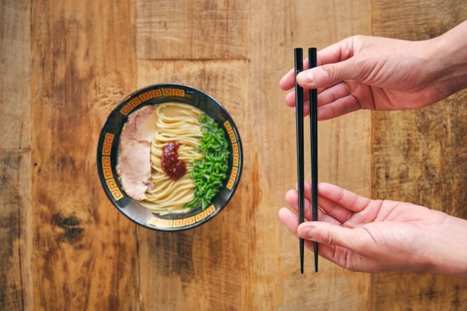 Crop person with chopsticks above tasty ramen on desk