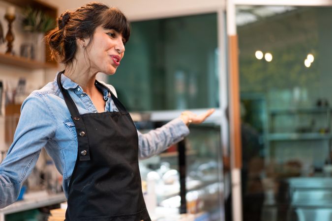 Woman wearing apron standing in cafe with arms opened