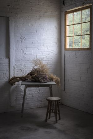 Bunch of plant in paper on table near stool in grey room