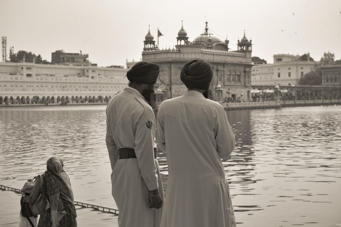 Grayscale photo of two men wearing turban standing beside body of water