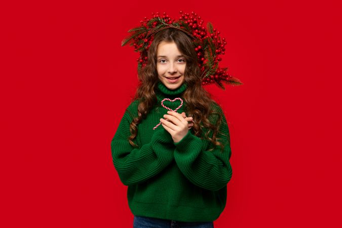 Girl in green sweater holding two candy canes shaped heart
