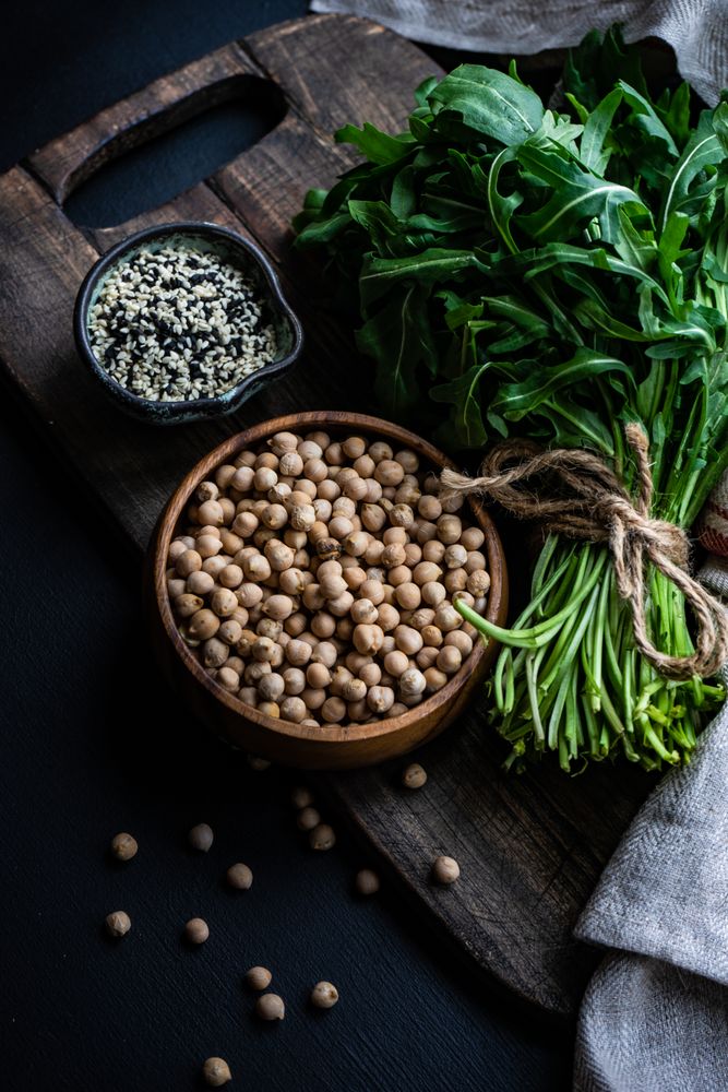 Bowl of garbanzo beans and sesame seeds next to arugula 