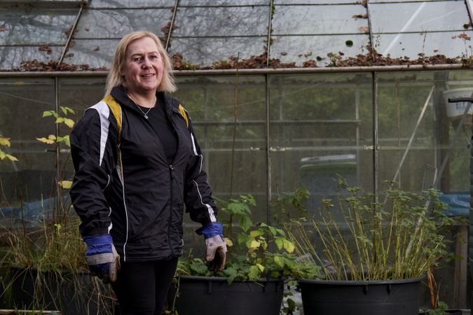Smiling woman with plants outside greenhouse with copy space