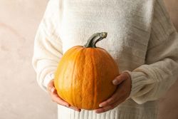 Young woman holding pumpkin on brown background, copy space
