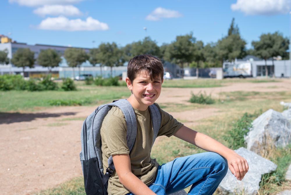 Smiling boy sitting on rocks outside with backpack