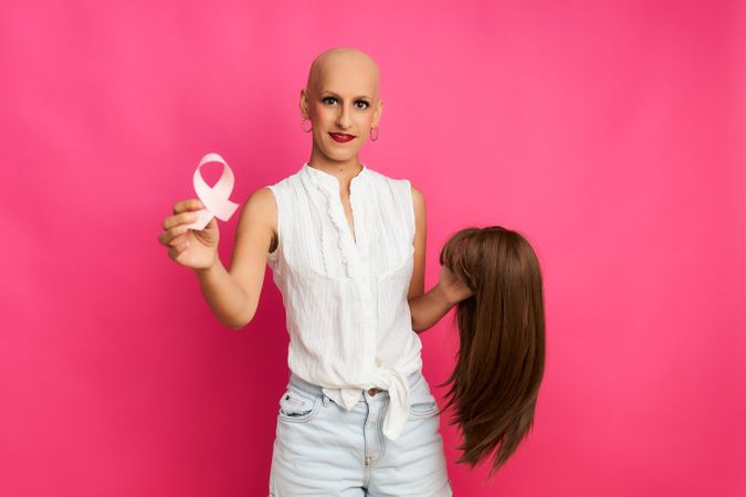 Woman suffering from cancer with a ribbon in her hand and holding a wig in the other hand