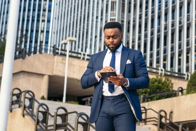 Low angle of a Black businessman in a suit using a tablet outside. He looks concentrated