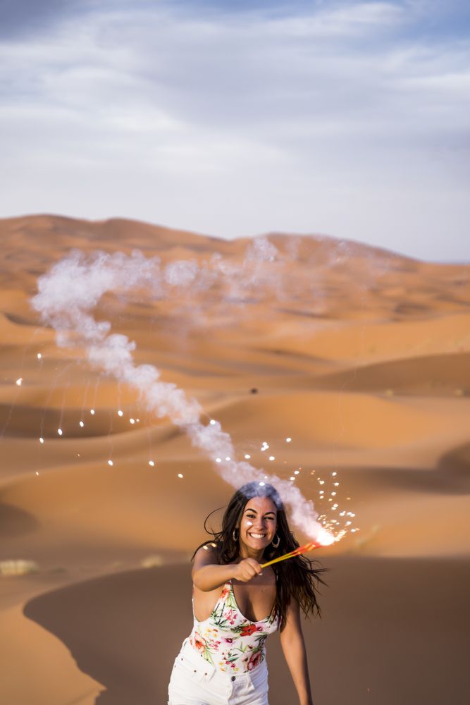 Happy woman holding firework in desert
