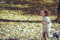 Playful child running in park of colorful fall leaves with her arms open