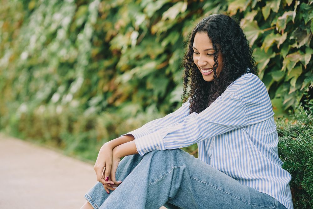 A Smiling Young Woman Sitting Outdoors, Surrounded by Lush Greenery in a Beautiful Setting