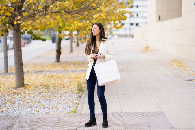 A young woman leisurely strolling down a beautiful autumn street, holding a shopping bag