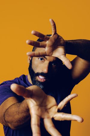 Serious Black man in yellow studio with fingers outstretched towards the camera