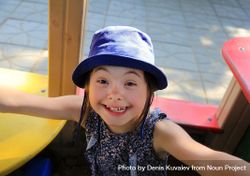 Portrait of little girl on the playground in a blue hat looking up at camera and smiling 4mDKB5