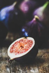 Figs, one halved, on wooden cutting board, close up