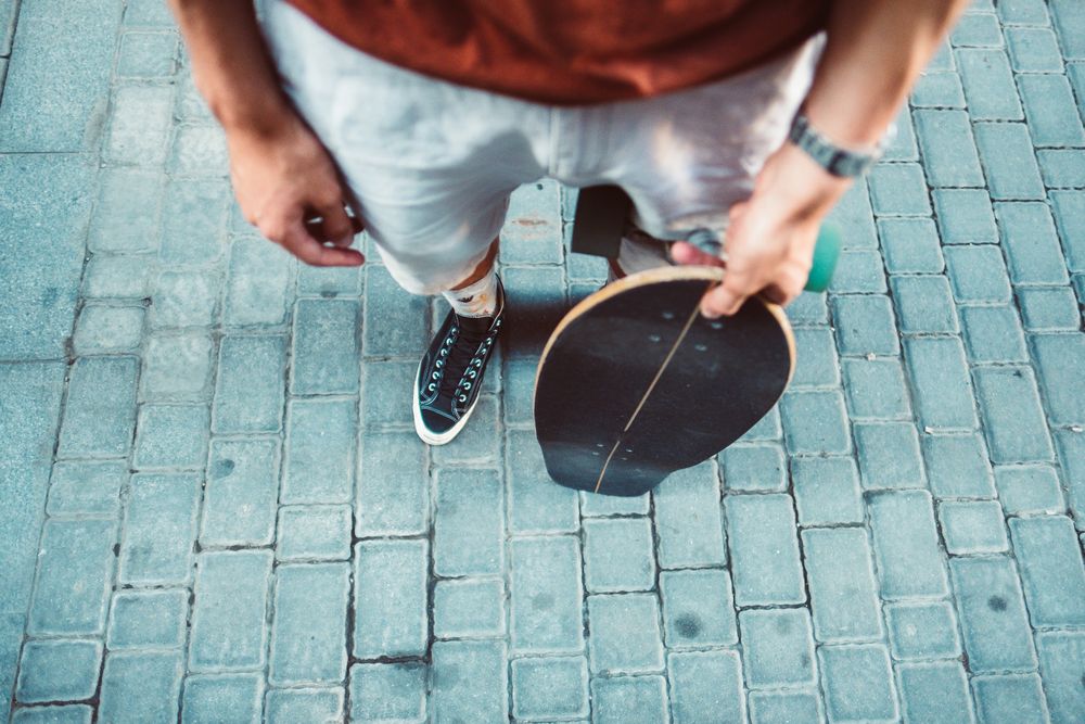 Sportive man carrying longboard while standing on street