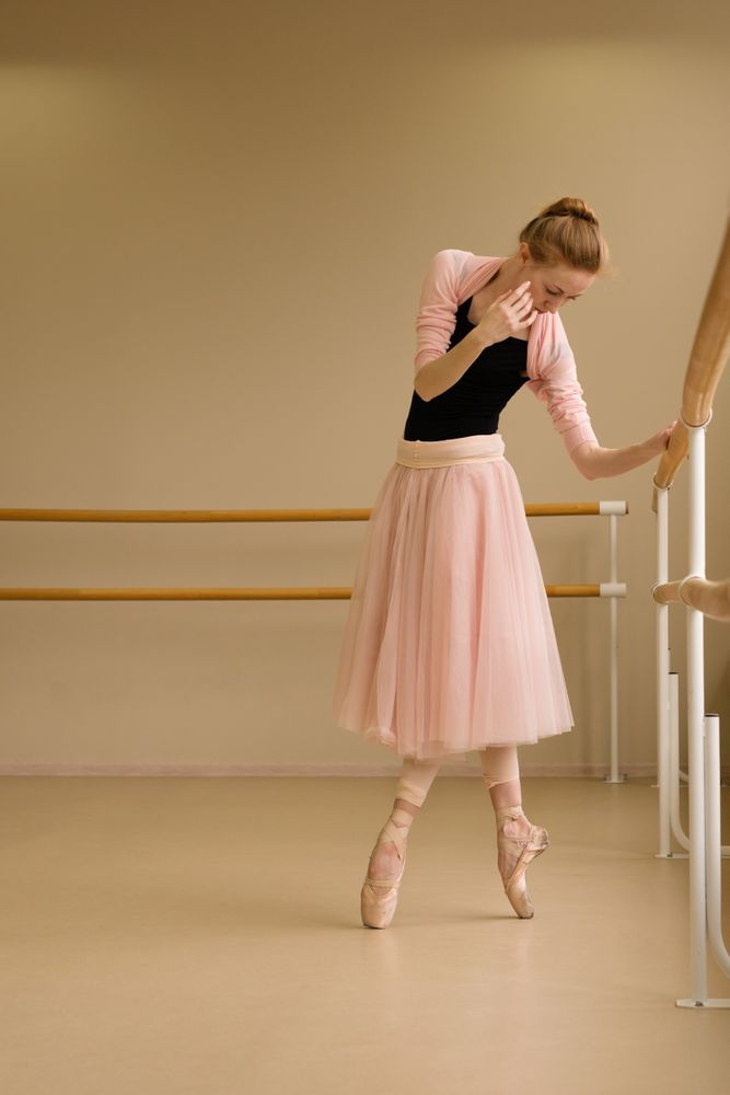 Ballet dancer resting hand on barre while standing en pointe