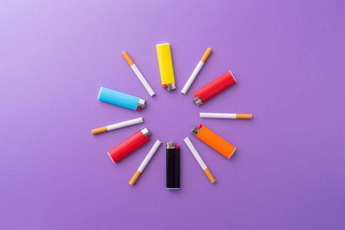Colorful lighters and cigarettes in a circle shape on purple background