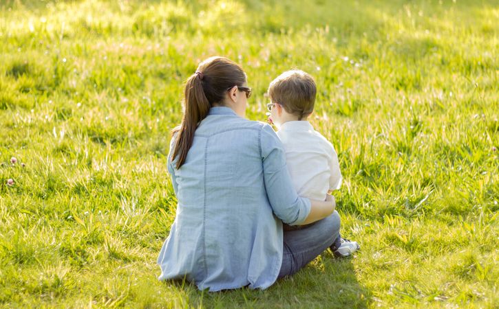 Cute son giving a bouquet of flowers to his mother sitting in a field