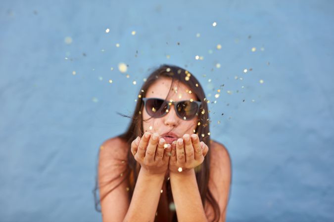 Portrait of beautiful young woman blowing glitter over blue background
