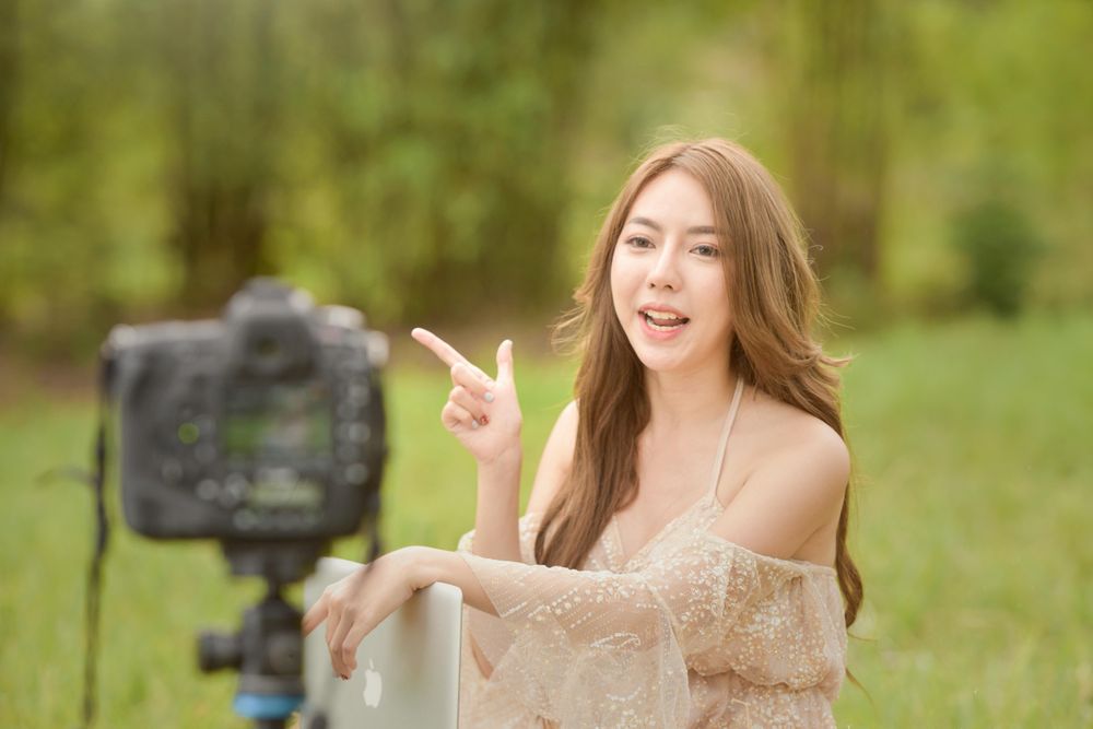 Woman video recording herself sitting on green grass