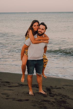 Amorous man carrying woman on arms along sandy beach