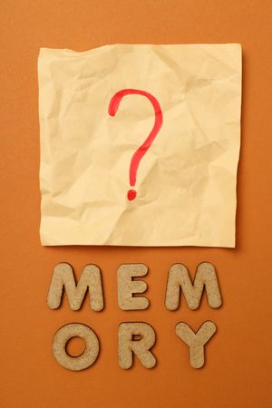 The word “Memory” written in cork below post it note on dusty orange background, vertical