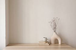 Table with modernist vase and decorative reeds, and coffee atop pile of books
