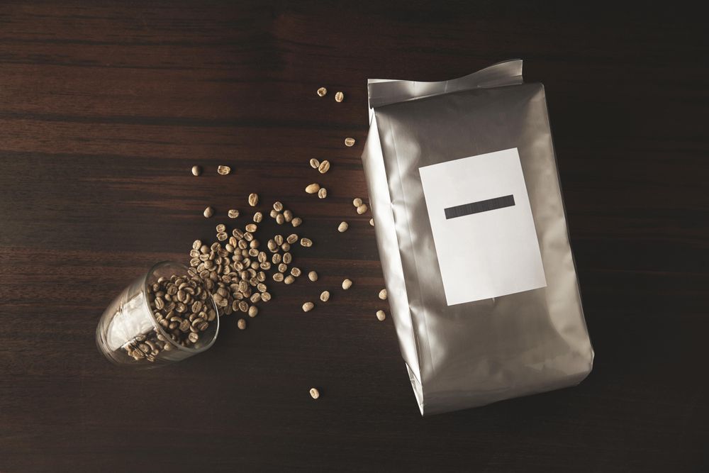 Bag of coffee beans with whole beans spilling out of small glass