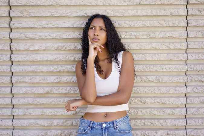 A Thoughtful Young Woman Posing Gracefully Against a Textured Wall in Natural Light