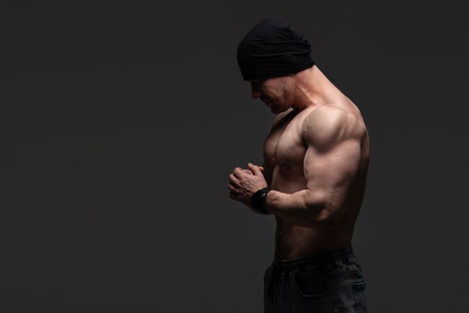 Shirtless muscular man in beanie with hands clasped