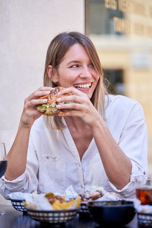 Smiling woman eating delicious burger in outdoors restaurant