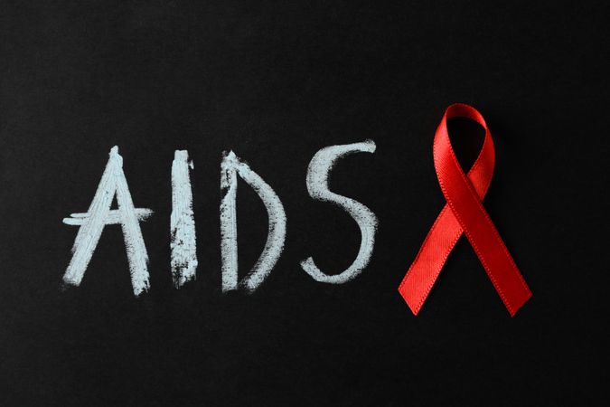 Awareness ribbon and inscription AIDS on dark background, space for text
