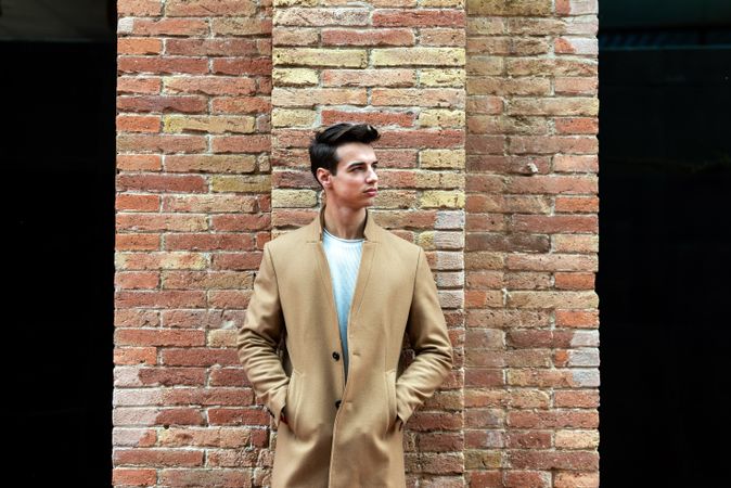 Young man standing on street with hands in camel coat pockets
