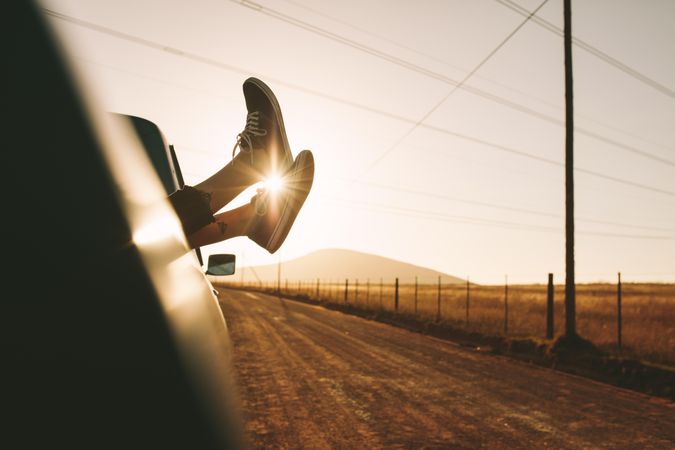 Legs hanging out from car with sun in the background
