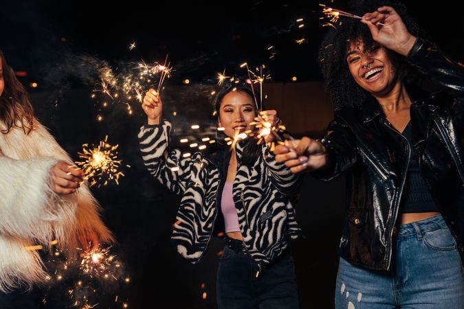 Three female friends smiling with sparklers at a party