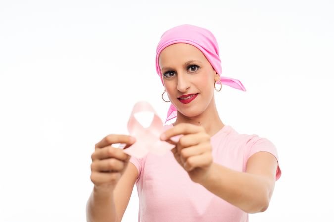 Smiling woman with cancer with pink headscarf holds ribbon bow in hand. Cancer awareness