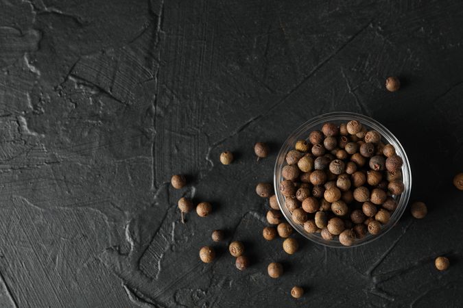 Top view of glass bowl with peppercorns on dark background with copy space