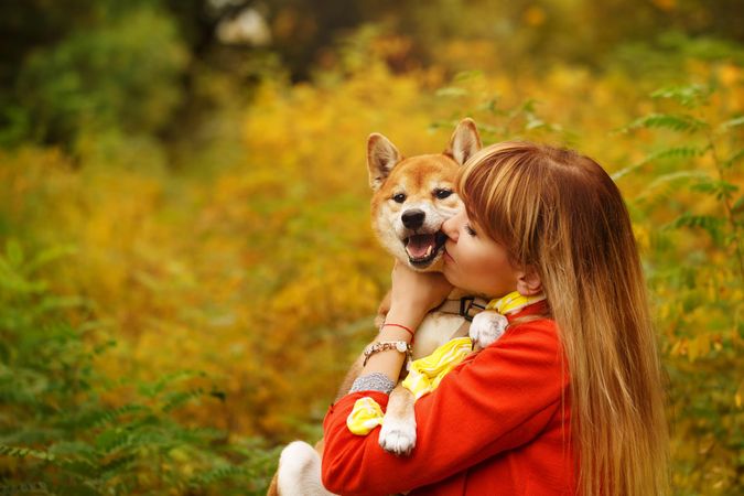 Female in red coat kissing her cute shibu dog standing in field