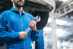 White male mechanic holding wrench at auto garage standing under lifted vehicle